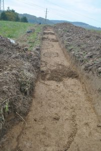 Widok na teren przeznaczony pod inwestycję przed przystąpieniem do badań wykopaliskowych, ale już po uzyskaniu głębokości zalegania obiektów. Widoczny długi wykop przed eksploracją obiektów archeologicznych.
